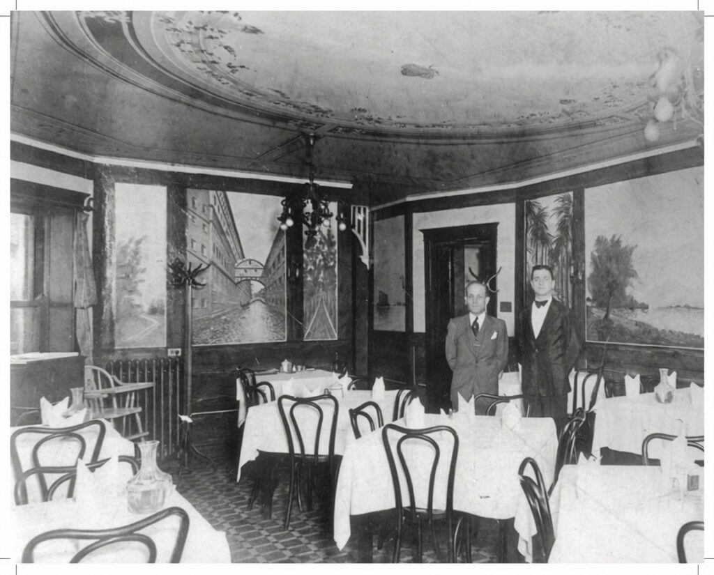 Restaurant table and chairs with waiter and manager in the back.