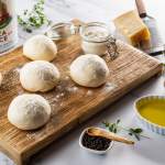 Fresh, never frozen pizza dough balls on a floured board with olive oil and seasoning