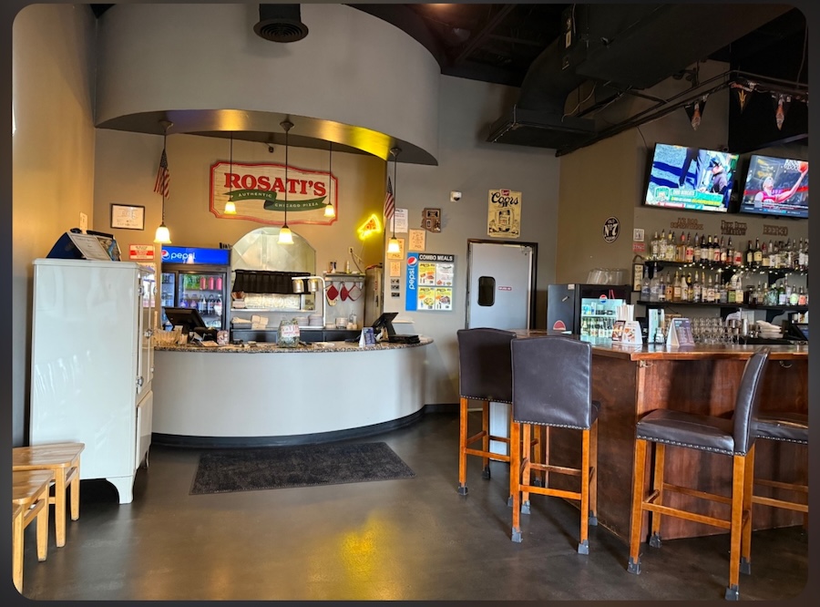 Interior of the Rosati’s Pizza restaurant in Gold Canyon, Arizona, featuring the front counter, Rosati’s signage, and a bar with high-top seating and TVs.