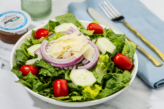 Salad with vegetables and cheese with a napkin fork and individual sized dressing container.